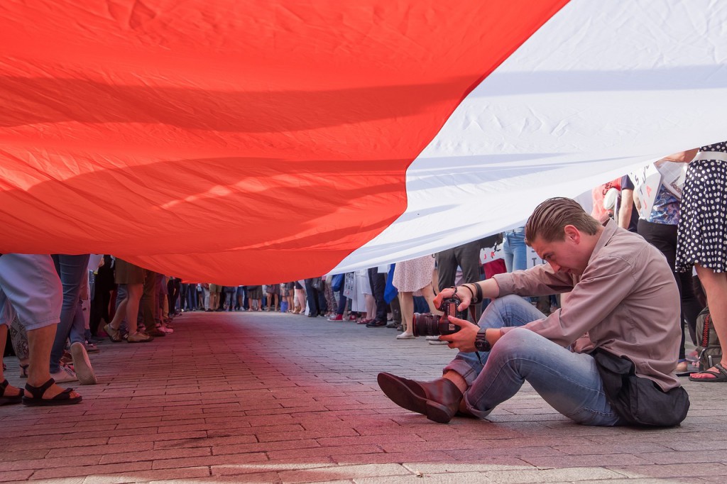 un manifestante tomando fotografías digitales bajo una bandera en una manifestación